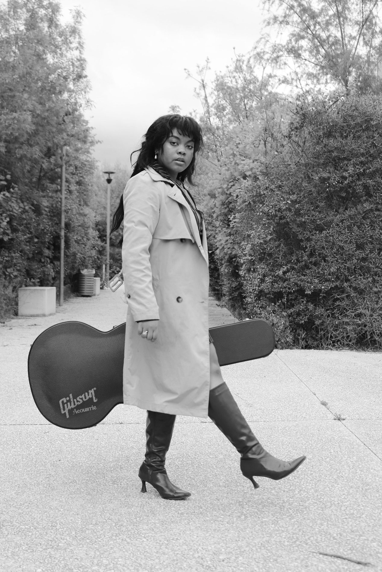 Rosa Zand en trench, étui de guitare Gibson, photo noir et blanc